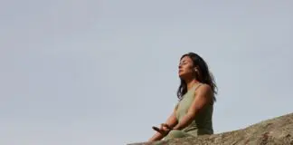 frau meditiert auf einem felsen vor blauen himmel
