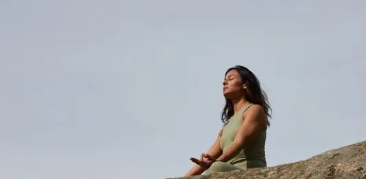 frau meditiert auf einem felsen vor blauen himmel