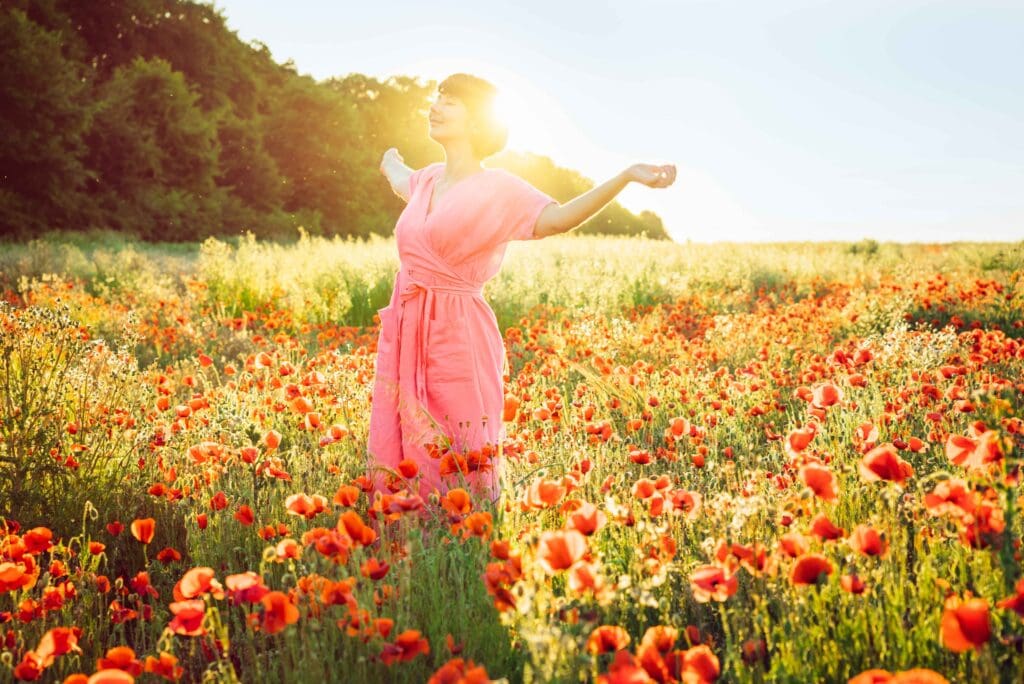 tanzende Frau im Sonnenlicht auf einer Blumenwiese, Symbolbild, von Oksana Krasiuk via Canva