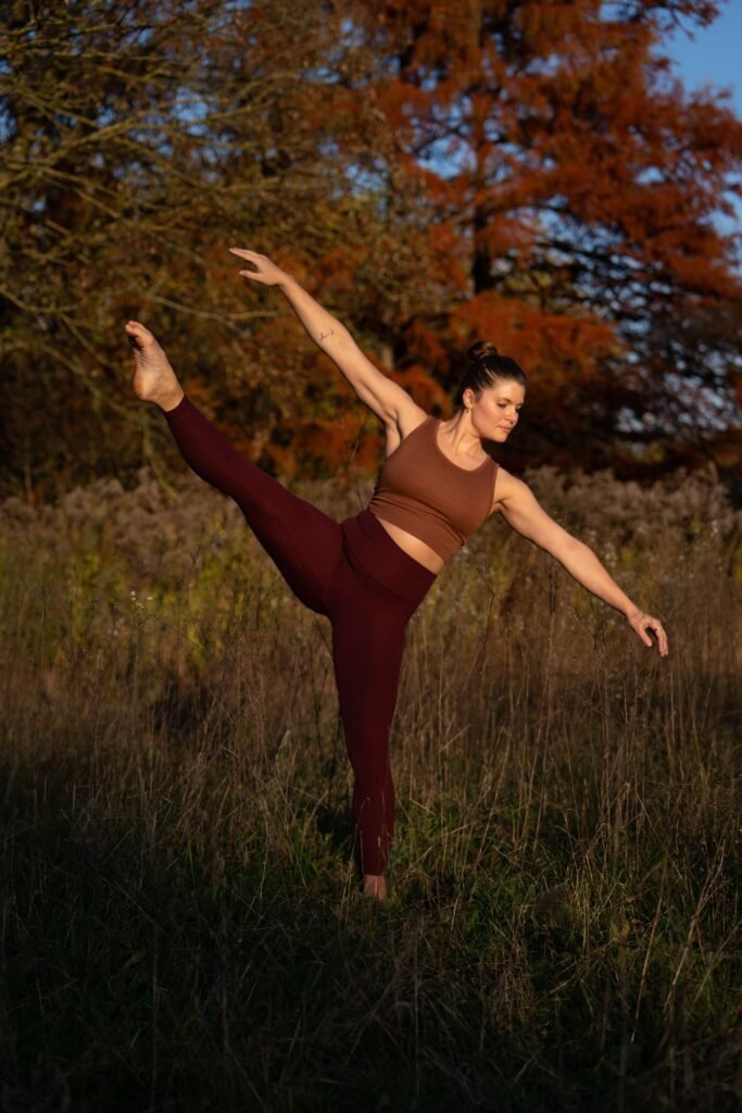 Daniela Mühlbauer, eine Frau tanzt in Yogakleidung draußen im hohen Gras, Chakra Journey, Yoga